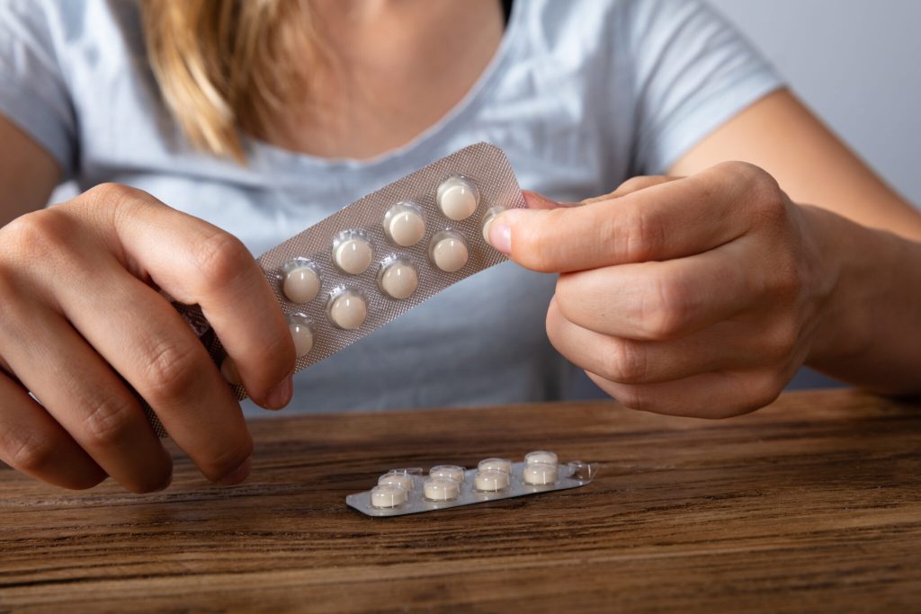Close-up Of A Woman's Hand Taking Medicine Over Wooden Desk